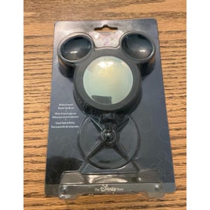 May include: A black Mickey Mouse-shaped computer monitor spy mirror in its original packaging. The mirror features a circular reflective surface, a stand with a four-pointed base, and the text Mickey Computer Monitor Spy Mirror on the card.
