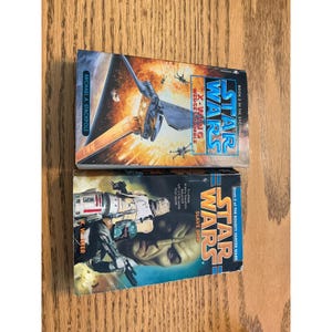 May include: Two Star Wars novels are displayed. The top book is titled "X-Wing Wedge's Gamble" by Michael A. Stackpole, featuring a space battle scene. The bottom book is "Slave Ship" by K.W. Jeter, with a depiction of Boba Fett.