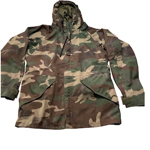 May include: Camouflage pattern jacket with a hood. The jacket features a mix of green, brown, and tan colors. It has a zipper closure, pockets, and adjustable cuffs. The jacket is designed for outdoor wear.