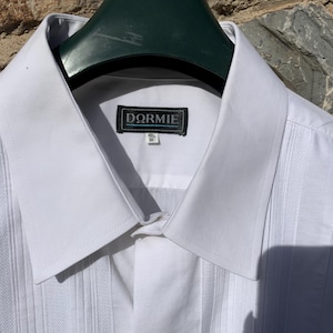 May include: White dress shirt with a classic collar and vertical textured panels. The shirt features a label that reads "DORMIE". The shirt is hanging on a green hanger.