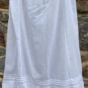 May include: White linen skirt with a detailed hem. The skirt features vertical seams and horizontal bands near the bottom, with a decorative eyelet lace trim. The fabric appears lightweight and suitable for warm weather.