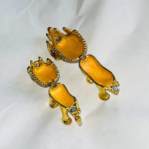 Puede incluir: Dos joyeros dorados con forma de zapatos de tac&oacute;n alto, con un interior amarillo brillante y peque&ntilde;as joyas. Las cajas con bisagras est&aacute;n abiertas, revelando el interior. Los zapatos est&aacute;n sobre una superficie blanca.
