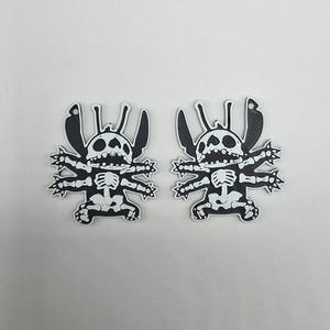 May include: Two black and white cartoon character skeleton-themed stickers. The stickers feature a stylized character design with a skeleton overlay. The character has large ears, a wide mouth, and multiple limbs. The stickers are on a white background.