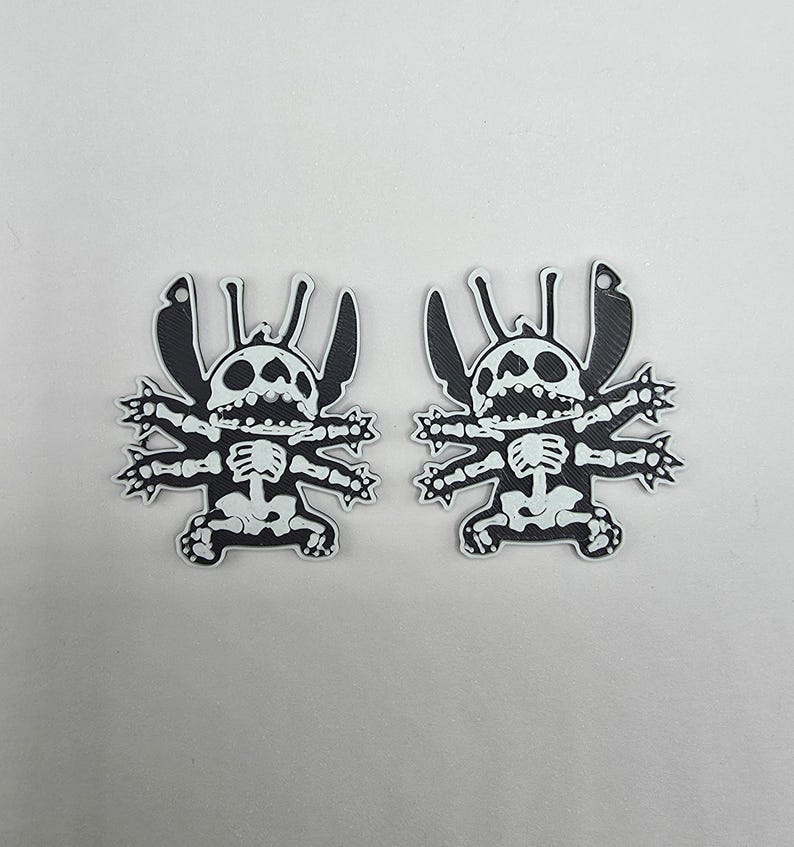 May include: Two black and white cartoon character skeleton-themed stickers. The stickers feature a stylized character design with a skeleton overlay. The character has large ears, a wide mouth, and multiple limbs. The stickers are on a white background.