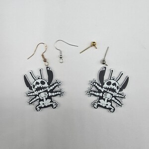 May include: A pair of black and white Stitch-themed earrings with a skeleton design. The earrings have a cartoon-style design and come with various earring hooks and posts. The earrings are displayed on a white surface.