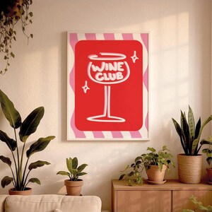 Puede incluir: Una impresión artística enmarcada con un fondo rojo, un diseño de copa de vino blanca y las palabras "WINE CLUB". La impresión está rodeada por un borde ondulado rosa y blanco y cuatro acentos de estrella.
