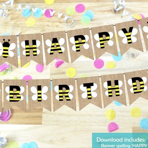 Puede incluir: Una pancarta de arpillera con las palabras "HAPPY BIRTHDAY" en letras negras con abejas rayadas de amarillo y negro y flores blancas. La pancarta está colgada en una superficie de madera con confeti de colores.