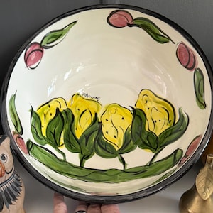 Może przedstawiać: Duża, ręcznie malowana ceramiczna miska z kremowym wnętrzem i czarną obwódką. Miska ma kwiatowy wzór z żółtymi kwiatami, zielonymi liśćmi i różowymi pąkami. Widoczny jest podpis artysty.