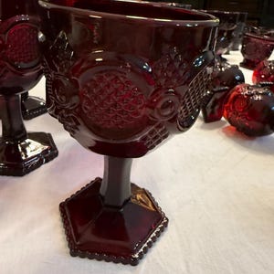Peut inclure: Ensemble de gobelets rouge rubis avec des motifs en relief ornés. Les gobelets ont une base hexagonale et un motif détaillé autour du bol. La verrerie est disposée sur une surface blanche, mettant en valeur sa couleur riche et ses détails complexes.