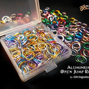 May include: A selection of colourful aluminium open jump rings, displayed in a clear plastic container. The rings are in shades of gold, silver, blue, purple, and green. Text reads "ALUMINIUM OPEN JUMP RINGS".