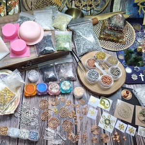 Könnte beinhalten: Eine Auswahl an Bastelmaterialien, darunter rosa Silikonformen, kleine Gläser mit bunten Perlen und Pulvern sowie verschiedene Metallanhänger und Spiralen. Die Artikel sind auf einer Holzoberfläche angeordnet, was auf ein Bastel- oder Schmuckherstellungsthema hindeutet.