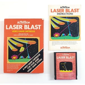 May include: An Activision Laser Blast video game cartridge for the Atari Video Computer System, including its original orange cardboard box and a printed instruction manual. The box and manual feature space-themed graphics with flying saucers.