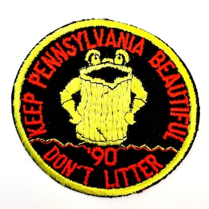 May include: A yellow and red embroidered patch with a cartoon frog wearing a trash can on its head. The text on the patch reads "Keep Pennsylvania Beautiful Don't Litter '90".