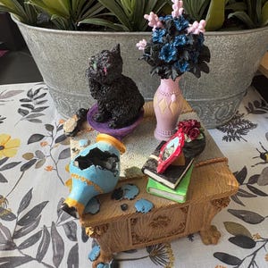 May include: A white ceramic mug with a black handle and the text "But First, Coffee" in a black, bold font. The mug is on a white surface. The mug is approximately 4 inches tall.