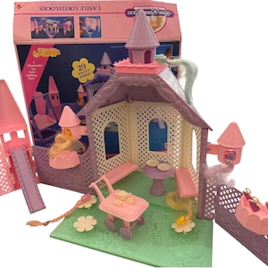 May include: A Castle Lovely Locks playset featuring a pink and lavender plastic castle structure with a green base, a pink serving cart, a small table with two plates, and various accessories. The original box is visible in the background with text.