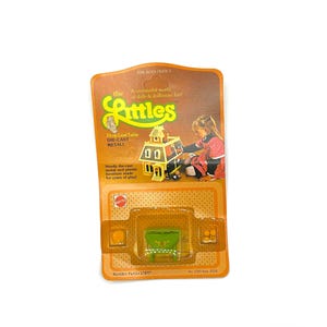 May include: Vintage Mattel "Littles" dollhouse furniture set on its original packaging. The packaging is orange and brown with the text "Littles" and "Drop Leaf Table". The set includes a green table and a miniature dollhouse.