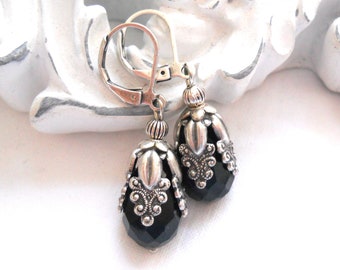 May include: A pair of silver dangle earrings with black faceted glass beads. The beads are surrounded by ornate silver filigree.