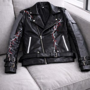 May include: Black leather jacket with a classic biker style. Features a notched collar, asymmetrical zipper, and a belted waist. The jacket has white and red embroidered lightning bolt designs on the sleeves and chest, and gray accents on the shoulders.