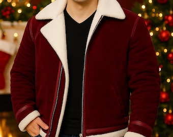 May include: A burgundy jacket with a white faux fur collar and trim. The jacket has a zipper closure and a black v-neck shirt underneath. The model is wearing blue jeans. The background includes a Christmas tree and a fireplace.