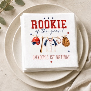 Könnte beinhalten: Ein Stapel weißer Papierservietten mit Baseball-Motiv und dem Text ROOKIE of the year! sowie JACKSON'S 1ST BIRTHDAY. Das Design zeigt einen roten Helm, einen Holzschläger, ein weißes Trikot, einen Baseball und einen braunen Handschuh an einer Leine.