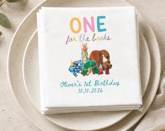 Op de afbeelding: Een stapel witte papieren servetten met de kleurrijke tekst ONE for the books, illustraties van een konijn, een vis, een rups en een beer met feesthoedjes, met de tekst Oliver's 1st Birthday en de datum 10.10.2026.