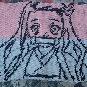 May include: Crocheted blanket featuring a character design. The top half is pink, the bottom half is white, and the character outline is black. The blanket is rectangular and appears to be handmade.