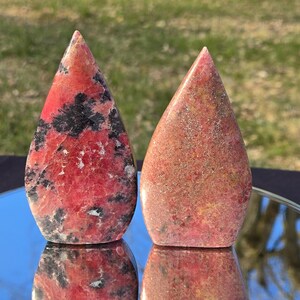 Pu&ograve; includere: Due pietre a forma di goccia con punte. La pietra a sinistra &egrave; principalmente rossa con inclusioni nere. La pietra a destra &egrave; un mix di rosso, marrone e giallo. Entrambe le pietre sono lucide e hanno una superficie liscia.
