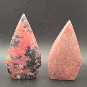Pu&ograve; includere: Due pietre a forma di goccia. Una pietra &egrave; un mix di rosso e nero con una punta bianca. L'altra pietra &egrave; di colore rosso-rosato uniforme. Entrambe le pietre hanno un aspetto liscio e lucido e sono su sfondo scuro.