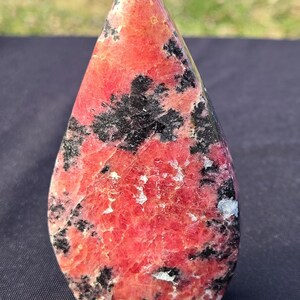 Pu&ograve; includere: Una gemma a forma di goccia lucidata. La pietra presenta una base di colore rosso vibrante, punteggiata da inclusioni nere e bianche. La parte superiore &egrave; appuntita e la forma generale &egrave; liscia e arrotondata. Ideale per la decorazione.