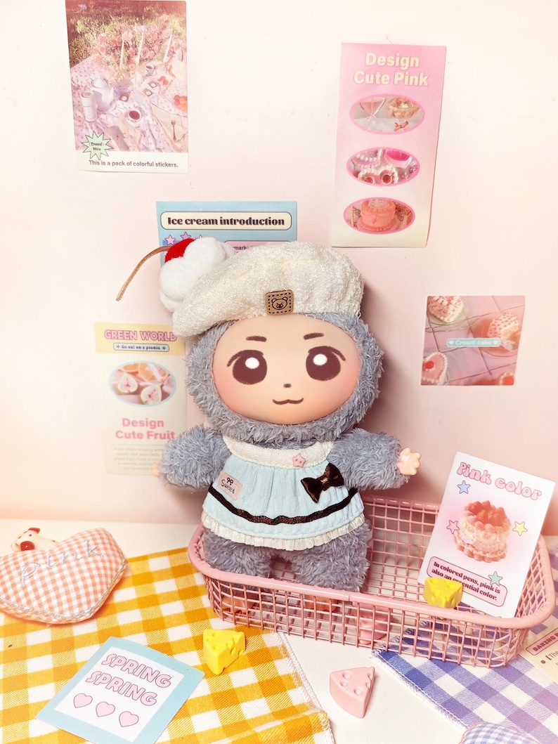 May include: A plush doll with a cartoon face, wearing a light blue dress and a white beret with a cherry on top, sits in a pink wire basket. The doll is surrounded by decorative cards and small toy food items. The text "SPRING SPRING" is visible.