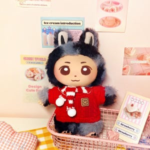 May include: A plush doll with a bunny ear hat and a red sweater with a white scarf. The doll is in a pink wire basket with a strawberry card. The background includes stickers and a pink heart-shaped pillow.