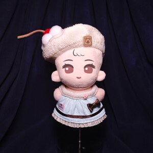 May include: A plush doll with a cream-colored hat adorned with a red and white cherry. The doll has a light blue dress with a brown bow and trim. The doll has a cute face with large eyes.