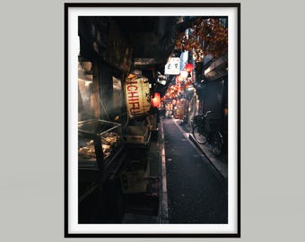 Op de afbeelding: Een ingelijste foto van een smalle Japanse steeg in de schemering. Rode lantaarns verlichten de straat, met een fiets aan de zijkant. De afbeelding legt de sfeer vast van een traditionele Japanse straatscène.