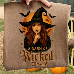 May include: A brown blanket featuring a witch with long red hair, winking and holding a finger to her lips. She wears a black witch hat and dress. The blanket has the text "A Dash of Wicked" with bats and a spiderweb design.