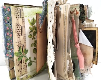 Puede incluir: Un diario hecho a mano con páginas de partituras, estampados botánicos y encaje decorativo. El diario presenta una variedad de texturas y colores, incluyendo cinta floral azul y un lazo rosa. Las páginas están encuadernadas con hilo.