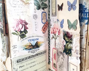 Puede incluir: Un diario de recortes abierto con páginas de collage que incluyen efímeros vintage, como un pase de Northern Pacific Railroad, una etiqueta de vino Verdon, ilustraciones botánicas de flores y mariposas, sellos y un retrato en blanco y negro.