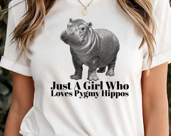 May include: White t-shirt featuring a grayscale illustration of a pygmy hippo. The text "Just A Girl Who Loves Pygmy Hippos" is printed below the hippo. The shirt has short sleeves and a crew neck.
