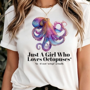 May include: White t-shirt with a vibrant octopus design in purple, blue, and yellow. The text states "Just A Girl Who Loves Octopuses*" and clarifies "No - it's not 'octopi' actually."