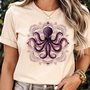 Op de afbeelding: Crèmekleurig T-shirt met een paars octopusontwerp in een mandala-patroon. De octopus heeft gedetailleerde tentakels en staat centraal op het shirt. De mandala is in tinten paars en roze.