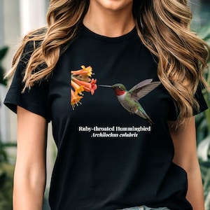 May include: Black t-shirt with a detailed illustration of a Ruby-throated Hummingbird feeding from orange and yellow flowers. The text "Ruby-throated Hummingbird Archilochus colubris" is printed below the image.