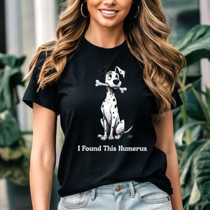 May include: Black t-shirt with a Dalmatian dog illustration holding a bone. The dog has black spots and is sitting upright. The text "I Found This Humerus" is printed below the dog.