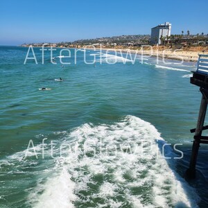 May include: A coastal scene featuring surfers, waves, and a pier. The sea is a vivid turquoise, and the sky is a clear blue. The text "Afterglow Pics" is visible across the image.