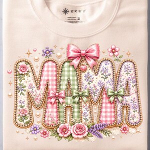 May include: A cream-colored crewneck sweatshirt featuring the word MAMA in large, decorative letters. The letters are filled with pink gingham, green gingham, and floral patterns, accented with small bows, pearls, and pink rose illustrations.