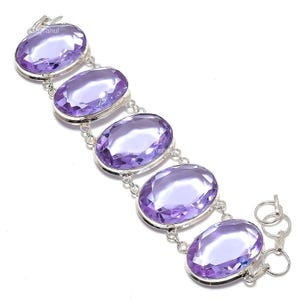 Könnte beinhalten: Ein Silberarmband mit fünf großen, ovalen, facettierten violetten Amethyst-Edelsteinen, die in polierten Metallfassungen sitzen. Die Steine sind durch kleine Silberglieder miteinander verbunden und das Stück hat einen runden Verschluss.