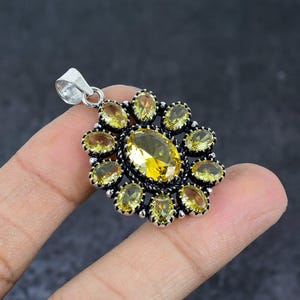 Könnte beinhalten: Silberner Anhänger mit einem großen, oval geschliffenen gelben Edelstein in der Mitte, umgeben von kleineren, oval geschliffenen gelben Edelsteinen. Der Anhänger hat ein Blumenmuster und eine silberne Öse für eine Kette.