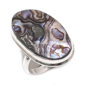 Könnte beinhalten: Ein ovaler Ring mit einer Einlage aus poliertem Abalone-Muschelmaterial, das wirbelnde Muster in schillernden Violett-, Braun- und Cremetönen aufweist. Die Muschel ist in ein glattes, poliertes Band aus silberfarbenem Metall eingefasst.