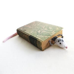 May include: A knitted bookmark shaped like a small gray and white mouse peeking out from behind a vintage book titled "Trees". The bookmark has a pink tail.