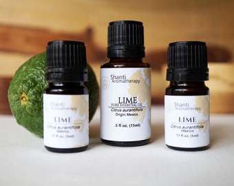 May include: Three amber glass bottles of lime essential oil with white labels. The labels have the text "Shanti Aromatherapy" and "LIME" with the botanical name "Citrus aurantifolia". The bottles are on a white surface with a green lime fruit in the background.