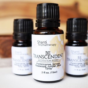 May include: Three small brown glass bottles with black caps and white labels. The center bottle label reads "Shanti Aromatherapy Be Transcendent Meditation Blend Frankincense, Spruce, Rosewood, Juniper, Blue Tansy .5 fl oz. (15ml)"
