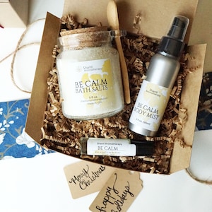 Puede incluir: Una caja de regalo con productos de aromaterapia "Be Calm", que incluye sales de baño, bruma corporal y una mezcla relajante en roll-on. El conjunto se presenta en una caja de cartón con papel decorativo y etiquetas de regalo.